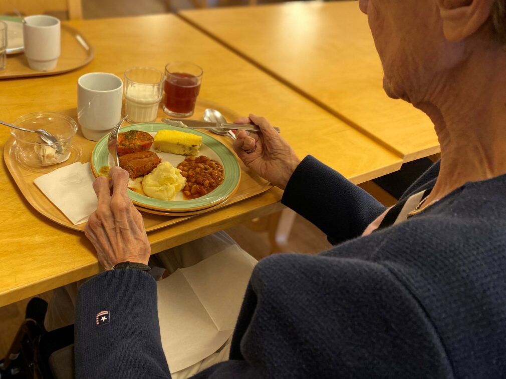 En äldre kvinna som sitter med en måltid framför sig.
